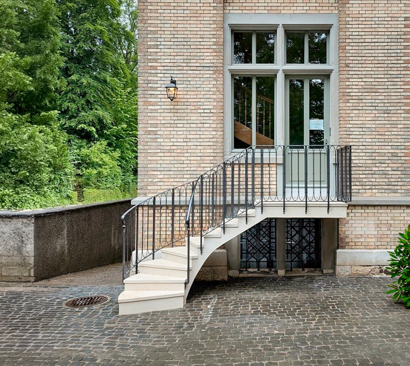 Steintreppe mit schwarzem Geländer vor einer Backsteinfassade und einem großen Fenster
