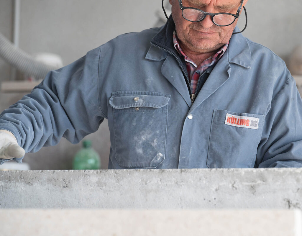 Arbeiter in blauer Arbeitsjacke bei der Arbeit an einer Steinplatte