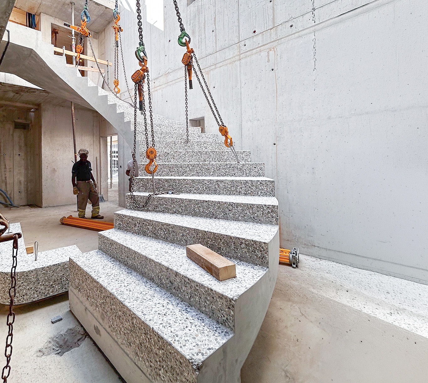 Treppenlauf aus Beton wird mit Ketten und Hebezeugen in einem Rohbau montiert