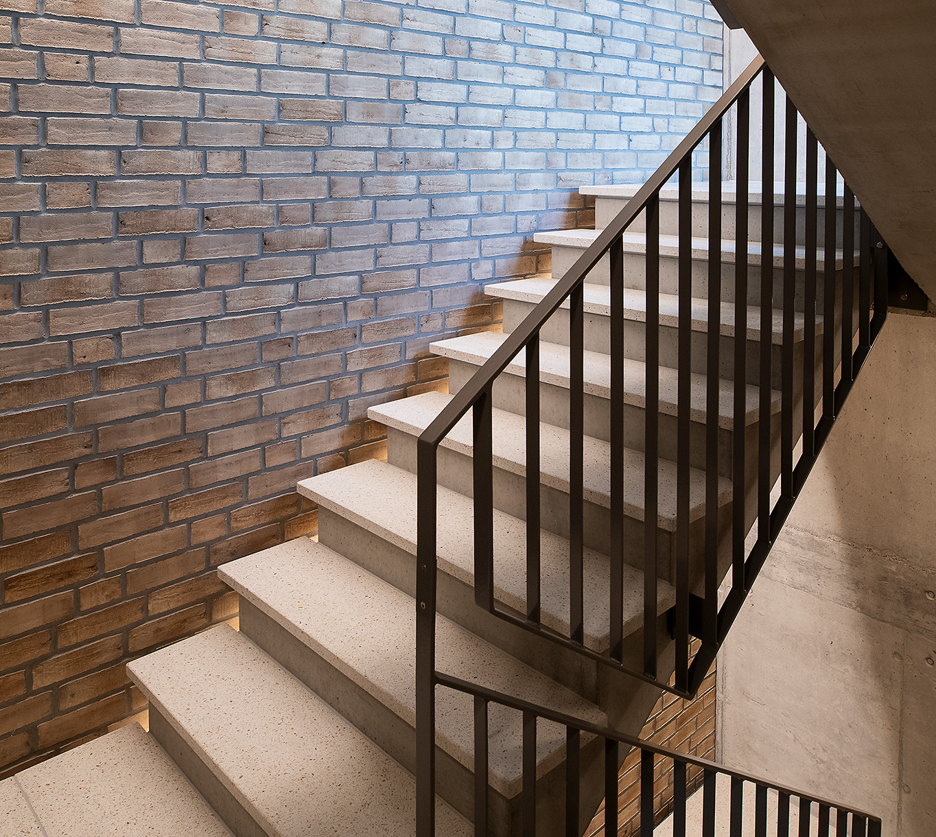 Betontreppe mit schwarzem Geländer neben einer Backsteinwand