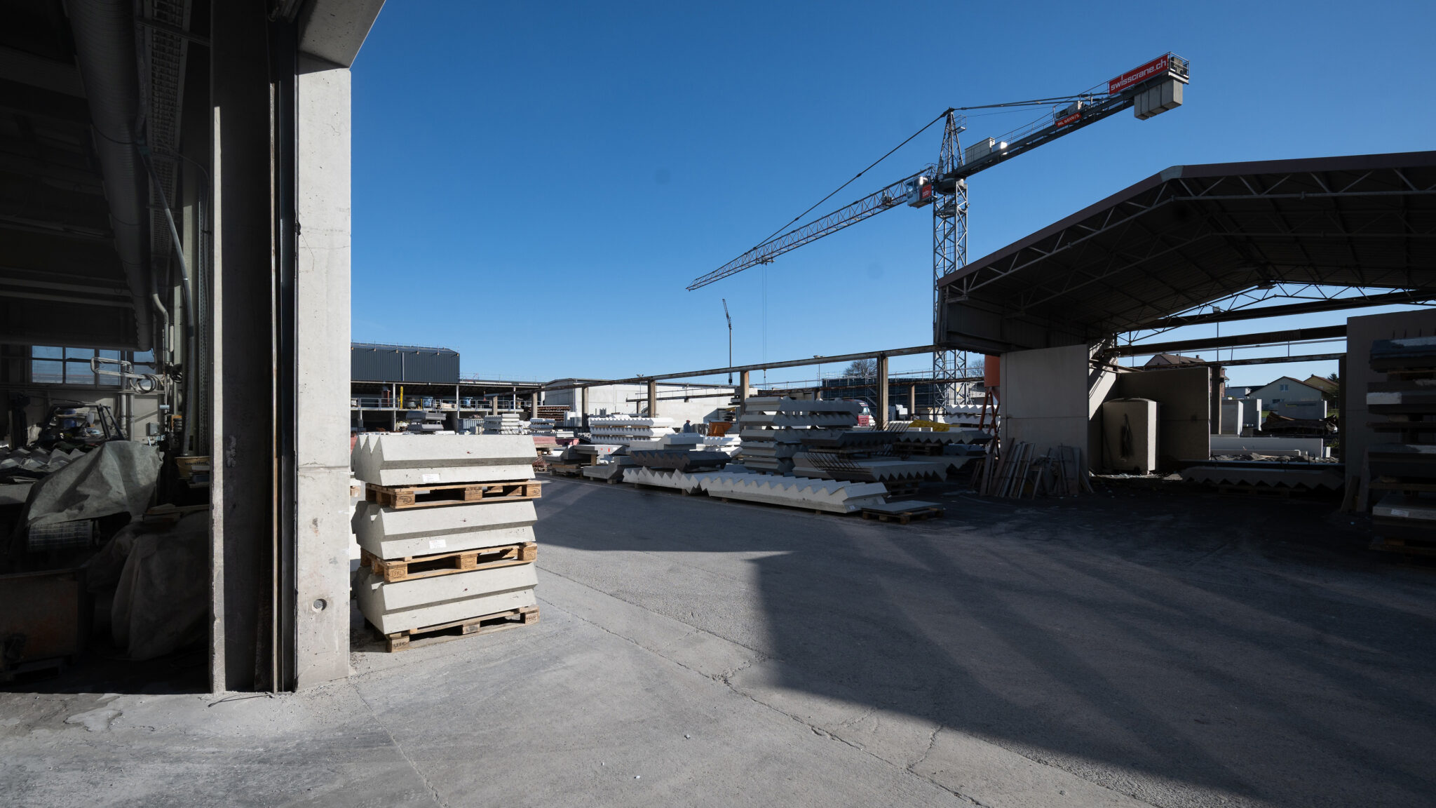 Baustellenlager mit Betonfertigteilen und Kran unter blauem Himmel