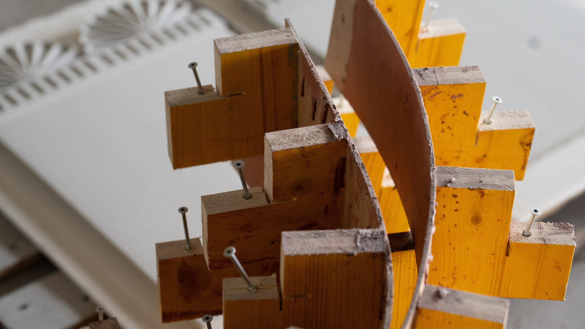 Holzmodell mit gestapelten, gelb lackierten und verschraubten Bauteilen