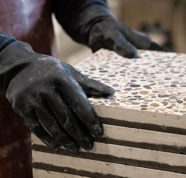 Mit schwarzen Handschuhen gehaltene Terrazzo-Platte mit sichtbaren Schichten