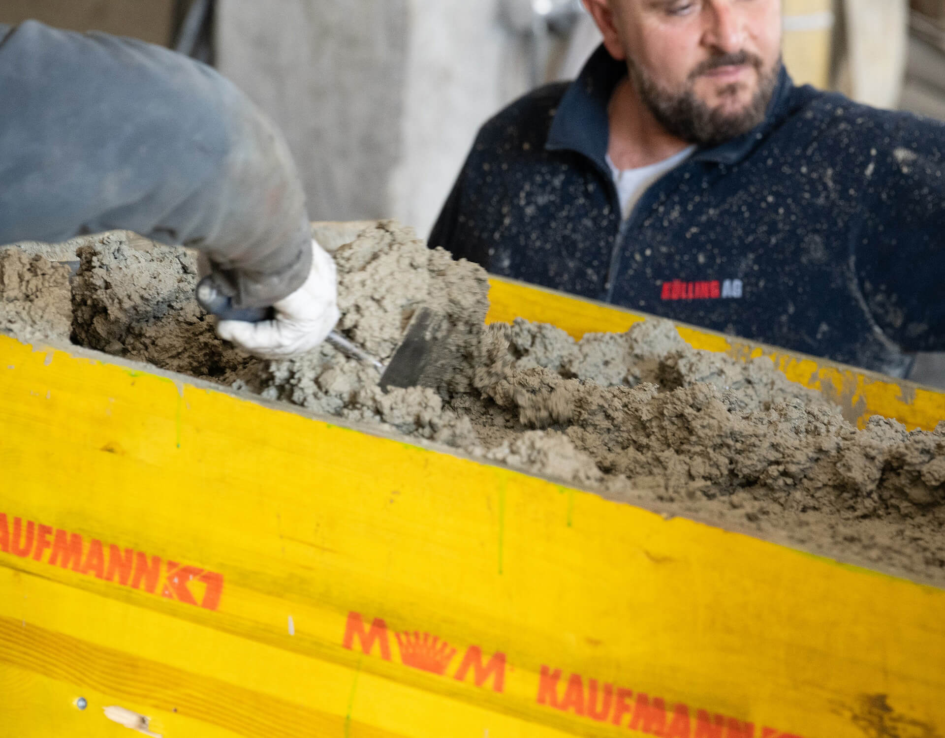 Arbeiter glätten Mörtel in einer gelben Schalung mit der Kelle