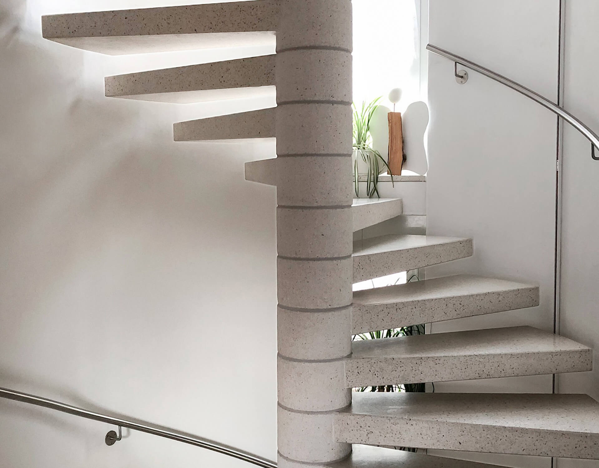 Betontreppe mit schwebenden Stufen und Edelstahlhandlauf in einem hellen Innenraum